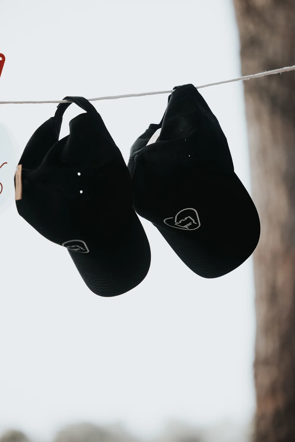 Two black caps hanging on a line, each carrying the mark in white